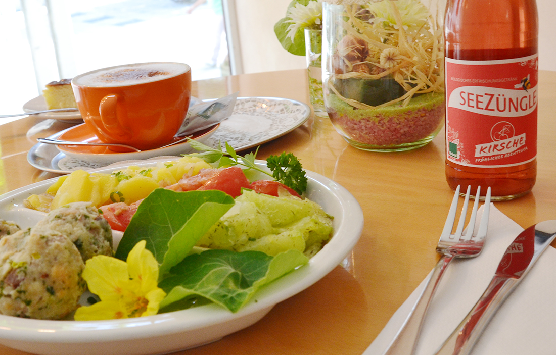 Bunter Teller mit frischem Salat, Kräuterknödeln und Gemüse, serviert mit Cappuccino und Seezüngle Bio-Kirschlimonade auf einem gedeckten Tisch im Staufen Suppentöpfle in Göppingen.